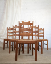 Load image into Gallery viewer, A set of six wooden ladder-back dining chairs with woven cane seats, arranged in a row against a white brick wall and draped white fabric.